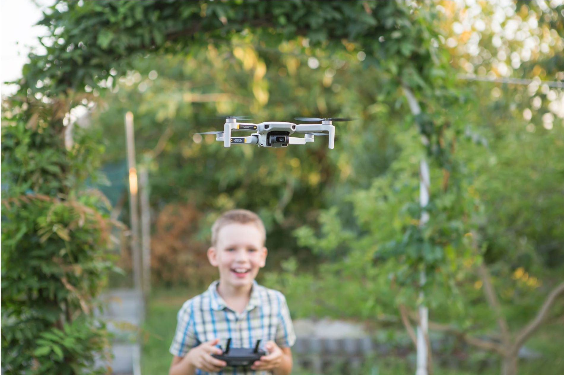 A young boy is smiling while flying a drone outside.