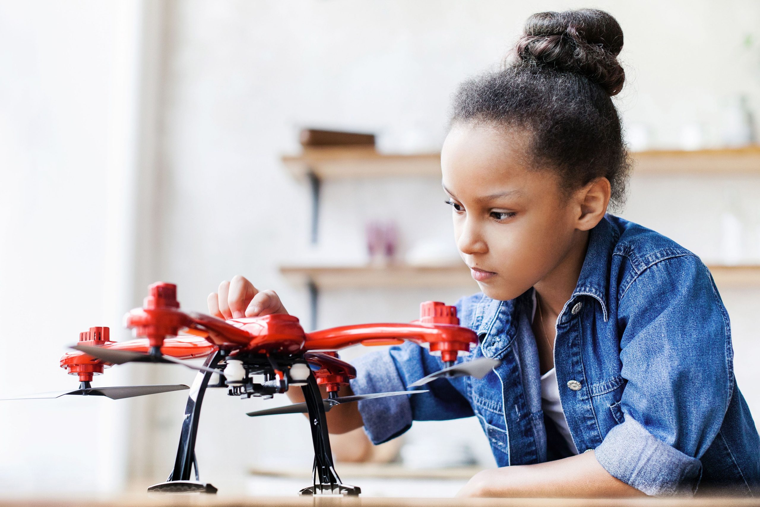 A young girl examining a red drone that is sitting on a table.