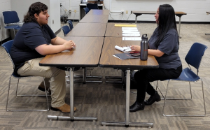 A student sits at a table across from someone else during a mock interview.