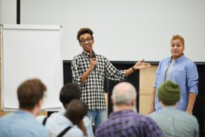 A young man is holding a microphone and speaking to a small group of people.