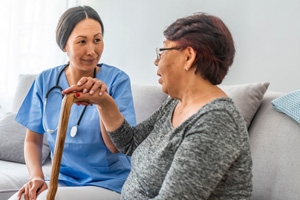 A woman wearing scrubs is sitting next to an elderly woman with a cane.