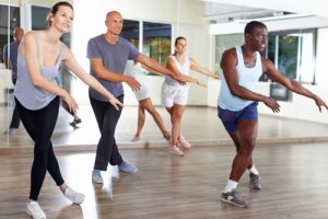 Four adults are in the middle of a dance/yoga move while standing in front of a mirror.