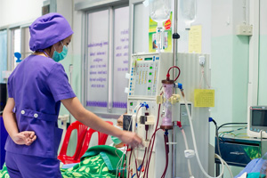 A nurse in purple scrubs is standing in front of a dialysis machine.