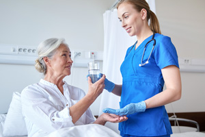 A young nurse hands a vile of medicine to an older woman sitting in a hospital bed.