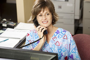 A woman wearing scrubs is smiling while answering the phone.