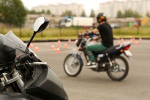 A young person is sitting on a motorcycle surrounded by small orange cones.