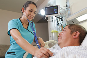 A nurse stands next to a hospital patient and listens to his heart beat with a stethoscope