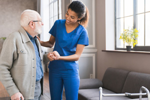 A young nurse is standing with an older gentleman in a lobby area, hands clasped.