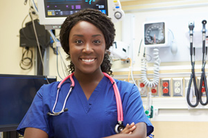 A nurse stands, smiling, with her arms crossed and a smile on her face. A stethoscope hangs around her neck.