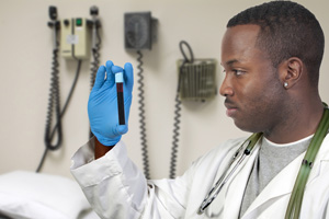 A doctor/nurse is looking at a vial while standing in a hospital room.